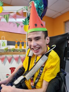 Image of a boy in a wheelchair, smiling with a fruit party hat on