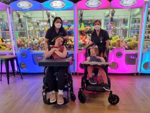 Two girls in wheelchairs with support staff outside of an arcade centre