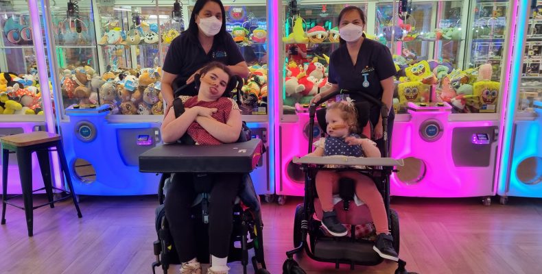 Two girls in wheelchairs with support staff outside of an arcade centre